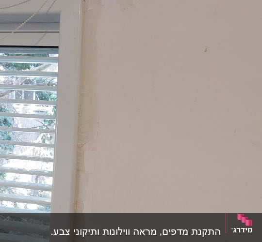 קיר עם תיקוני טיח ליד חלון עם תריסים